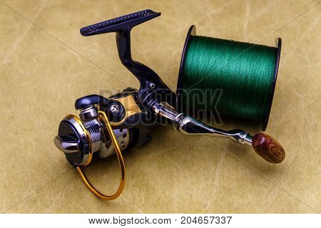 Fishing Reel And Spool Of Cord On The Background Of Tarpaulin. Green  Fishing Line. Fishing Reel And