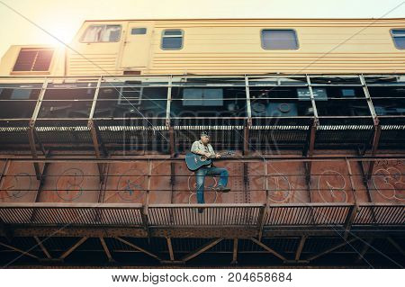 Bluesman with the guitar standing under a bridge on the background of a moving train.