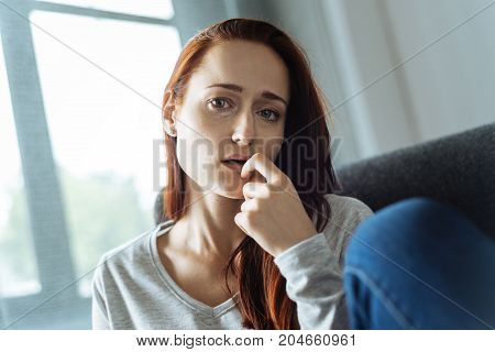 Too much stress. Unhappy cheerless red haired woman thinking about her problems and biting her nail while being nervous