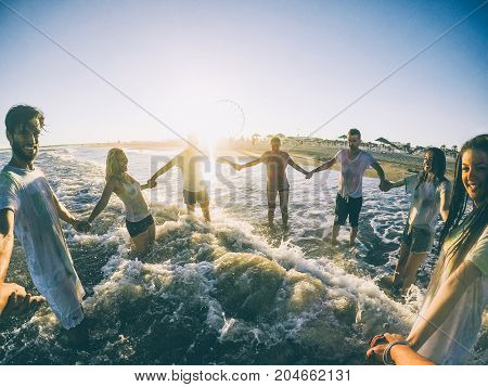 Pov view of happy friends having fun on the beach at sunset - Young people playing inside ocean in summer vacation - Friendship youthtravel concept - Soft focus on right woman and left man faces