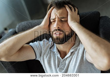 Stop this pain. Cheerless desperate unhappy man holding his head and closing eyes while suffering from pain