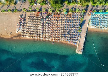 Aerial view of transparent turquoise sea, beautiful sandy beach with colorful chaise-lounges, boats, green trees at sunset in Icmeler, Turkey. Summer seascape. Top view from flying drone. Azure water