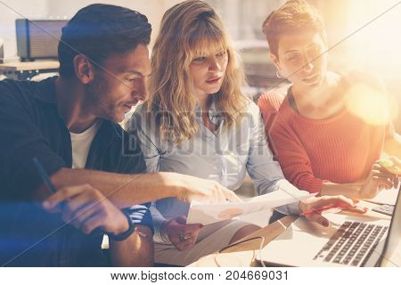 Teamwork process concept.Young coworkers team work with new startup project in office.Analyze document, plans.Modern laptop on wood table, papers, documents.Horizontal, blurred, flare.
