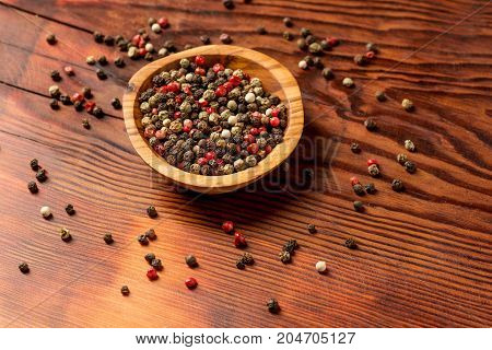 Peppercorns in a wooden bowl on a dark wooden background.
