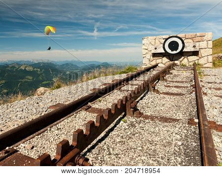 Endpoint of a rack railway on the top of a mountain on a sunny day with a paraglider in the background