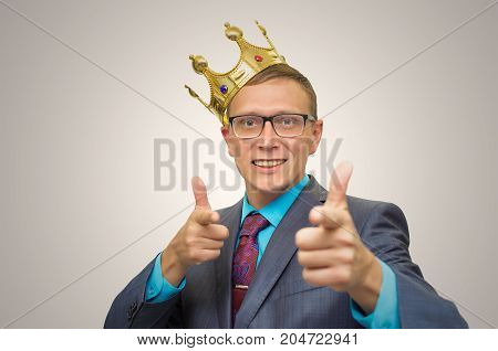 Winner. Award ceremony. First place man. Top manager. Young successful business man in suit and glasses with golden crown on his head showing success symbol. Vip client. Premium user. Success.