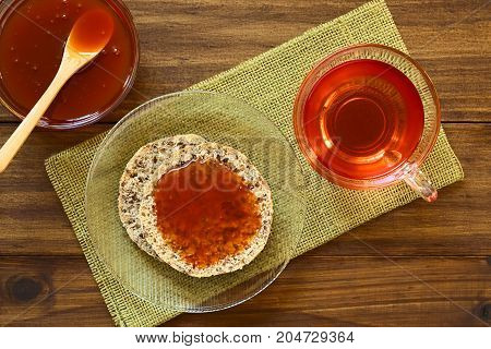 Homemade rose hip jam on wholegrain rolls with rose hip tea on the side photographed overhead on wood with natural light