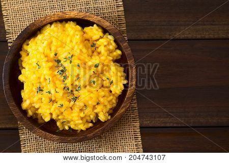 Pumpkin risotto prepared with pumpkin puree and sprinkled with fresh thyme leaves served in wooden bowl photographed overhead on dark wood with natural light (Selective Focus Focus on the top of the risotto)