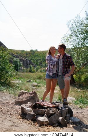 A young couple is traveling in the mountains. Summer journey of lovers, a guy frying meat at a bonfire for a girl. Healthy way of life, travel, summer vacation. The best pastime in the summer.