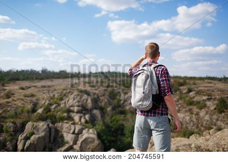 The guy looks into the distance, standing on the mountain. Beautiful mountain view on the background. Man in search of a way. Summer trip through the mountains without a map. Summer time.