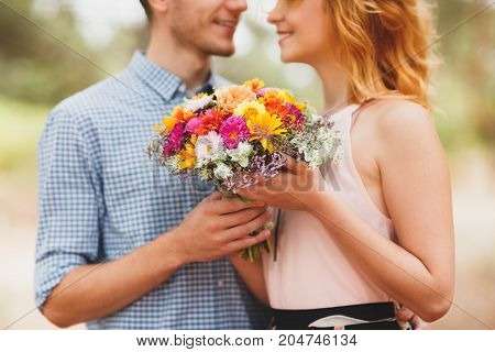 The guy gave his girl beautiful autumn flowers standing in the woods. A young couple are walking in a coniferous forest. Coniferous forest in the background. Background blur. Great time for a walk