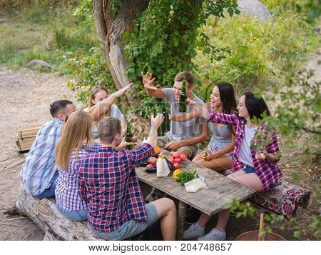 Young people having fun near the canyoun, drinking beers and chatting while their friends roast the meat on the bbq.