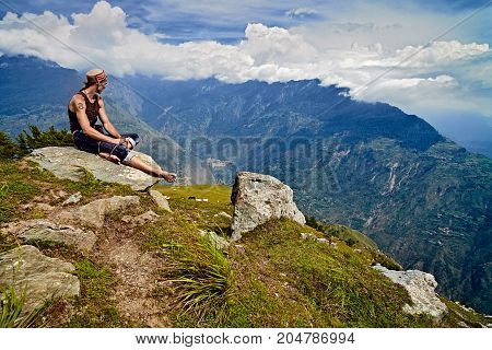 Man sits on mountain peak and looks down on the Kullu valley. Naggar, India - August 2017. Himachal Pradesh. North India.