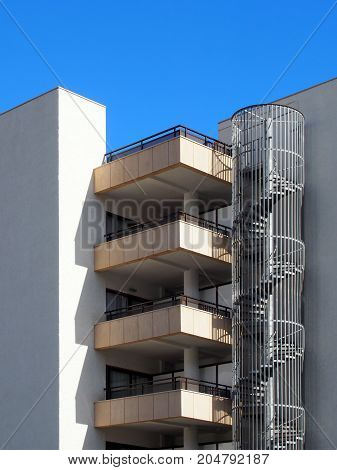 modern apartments detail with balconies spiral fire escape and white walls in sunlight with blue sky