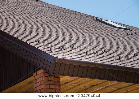 Tiled brown roof of new house with overflow, protection, from snow and fronton made of siding.