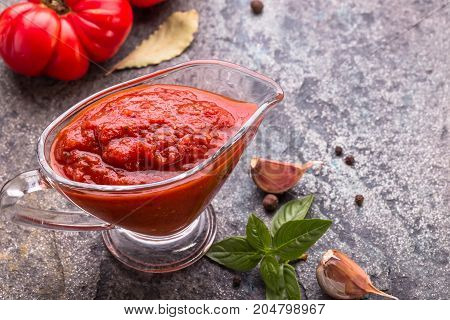 Tomato ketchup sauce with garlic and  basil  in gravy boat on stone background,  copy space