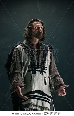 Actor in makeup, a poor man on black studio background. The bum in canvas rags. concept of vagrancy and survival