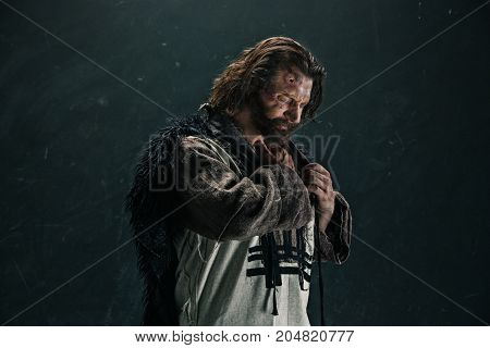 Actor in makeup, a poor man on black studio background. The bum in canvas rags. concept of vagrancy and survival. concept of pain and suffering