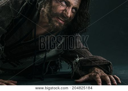 Actor in makeup, a poor man on black studio background. The bum in canvas rags. Concept of vagrancy and survival. Concept of pain and suffering. The wounded man crawling to salvation