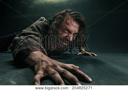 Actor in makeup, a poor man on black studio background. The bum in canvas rags. Concept of vagrancy and survival. Concept of pain and suffering. The wounded man crawling to salvation