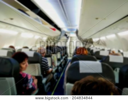 Blured view of the interior of modern commercial airplane with passengers on their seats waiting to taik off.