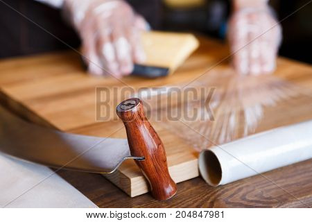 Grocery shop background. Shop assistant wrapping a piece of cheese. Packing order at grocery shop in cling film on wooden table, background