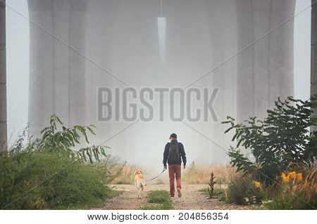 Man with dog under highway bridge in mysterious morning fog. Prague Czech Republic