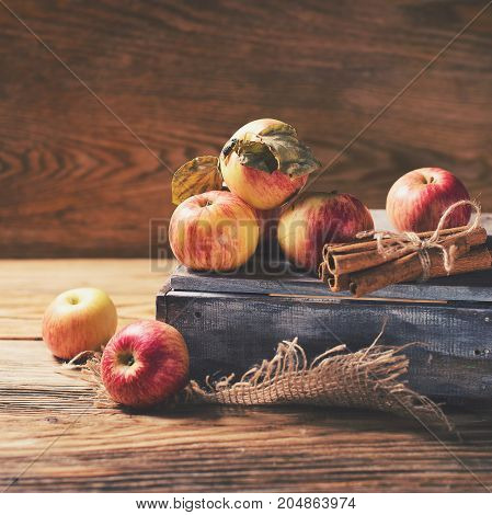 Box with ripe apples and cinnamom on wooden background. Copy-space