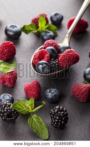 Ripe and sweet berries on vintage metal spoon on black table