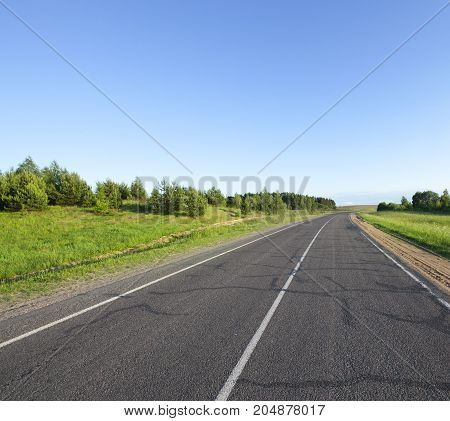 A Small Asphalt Road In The Summer. The Roadway Is Divided By A White Line Of Road Markings For Traf