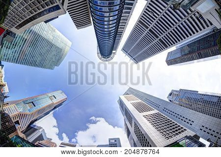 Bottoms-up view of business office skyscrapers and highrise buildings in Singapore's business and financial district at Raffles Place. Fisheye shot of rising architecture into blue and cloudy skies.
