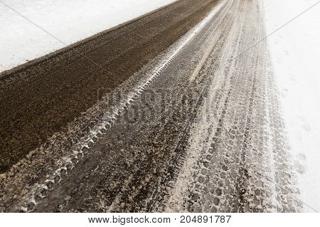Melted Snow On The Car Paved Road In The Winter Season. On The Snow Prints Of The Car Tires Are Visi