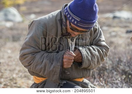 tsaatan man carving a reindeer horn outdoors in northern Mongolia