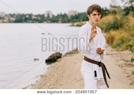 Young professional karate fighter in a blocking position. Boy on a jui-jitsu training on a blurred natural background.