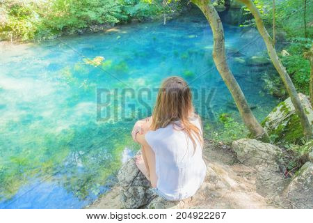 Young woman sitting near the beautiful lake in nature.
