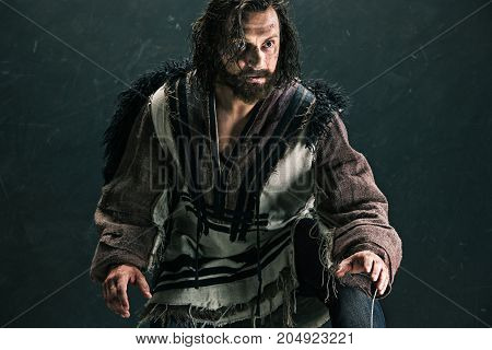 Actor in makeup, a poor man on black studio background. The bum in canvas rags. concept of vagrancy and survival