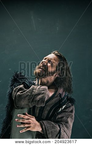 Actor in makeup, a poor man on black studio background. The bum in canvas rags. concept of vagrancy and survival