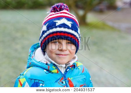 Portrait of happy cute little kid boy in colorful warm winter fashion clothes. Funny child having fun in winter forest or park on cold day.