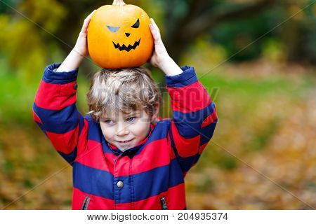 Happy cute little kid boy with halloween pumpkin lantern. Funny child in colorful clothes having fun and playing in autumn garden on cold autumnal day. Scary jack-o-lantern, celebration of holiday