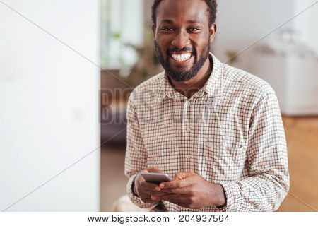Mood-boosting conversations. Handsome cheerful man exchanging text messages with his friends and smiling happily at the camera