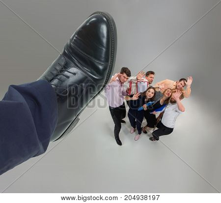Scared and shocked team of young business men and women under boss pressure. Concept horror and fear of the boss. Collage with big shoe of boss