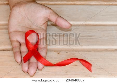 The symbolic conception of the world day of fight against AIDS. The red ribbon in the hands of a woman on wooden background.