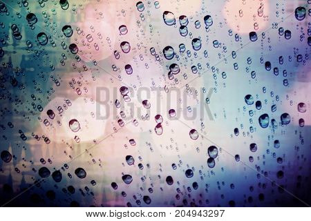 Raindrops on glass with light bokeh rainy seson abstract background.