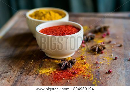 Close up two bowls filled with red paprika and yellow turmeric powder on dark wooden table covered with anise