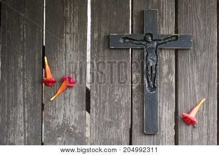 Black Wooden Crucifix On The Shabby Wooden  Plank With Red Flowers.