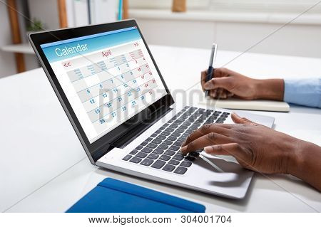 Close-up Of Businesswoman Writing Schedule In Calendar Diary On Desk