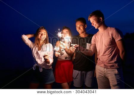 Friends Walking, Dancing And Having Fun During Night Party At The Seaside With Bengal Sparkler Light