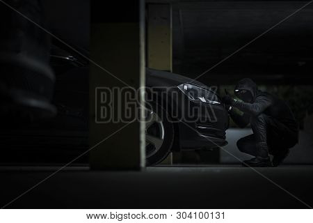 Caucasian Car Thief On A Parking Lot Trying To Open Modern Compact Car Hood To Get Access To Alarm D
