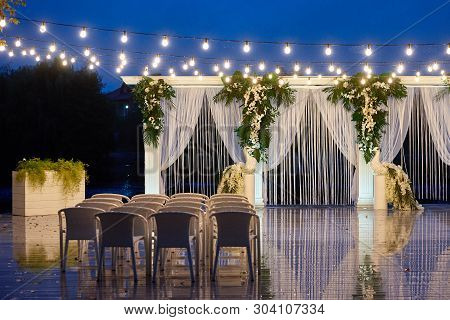Night Wedding Ceremony With Arch, Orchid Flowers, Chairs And Bulb Lights In Forest Outdoors, Copy Sp