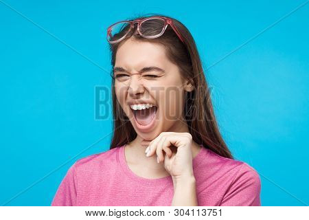 Studio Shot Of Young Female Winking While Flirting, Isolated On Blue Background